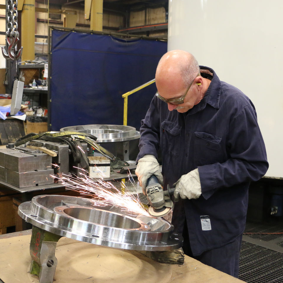 CNC Machinist using a grinder to grind off the burrs from the A- End Bearing Housing to prep for next operation on the machine at the Sovereign Road location.